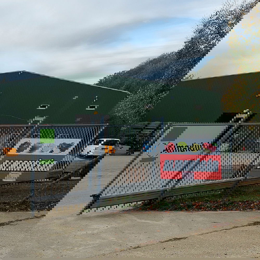 Das erweiterte Almakúti-Gelände, von außen fotografiert. Eine grüne Halle hinter einem offenen Tor, an dem das Almakúti-Logo hängt.