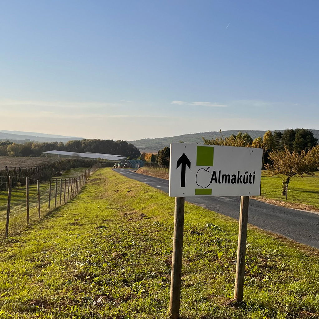 A signpost of Almakúti alongside the beautiful apple orchards, with a view of the farm shop in the distance.