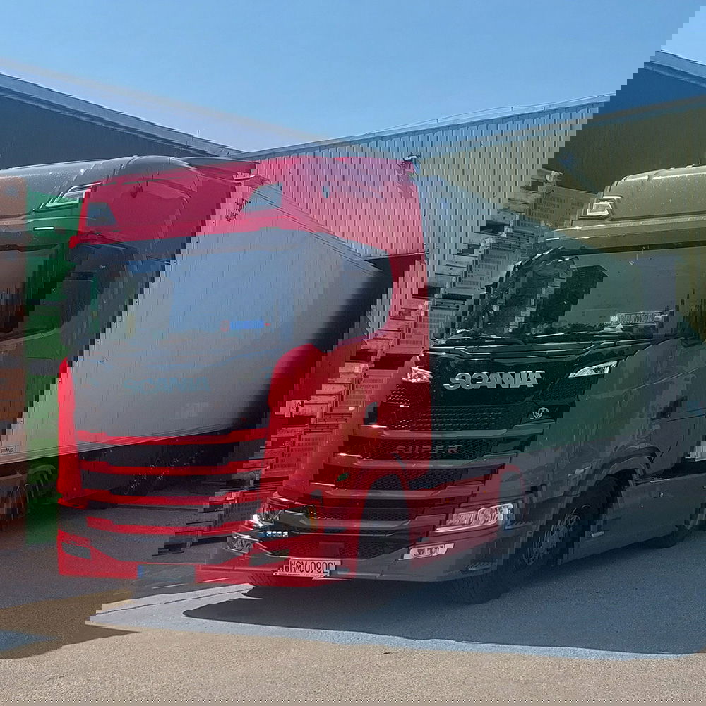 Een rode Scania-vrachtwagen met een witte oplegger staat gedeeltelijk in een laad- en losruimte van Almakúti gereden. Op de achtergrond bevinden zich groene en houten kratten, die worden gebruikt voor het transport van het fruit.